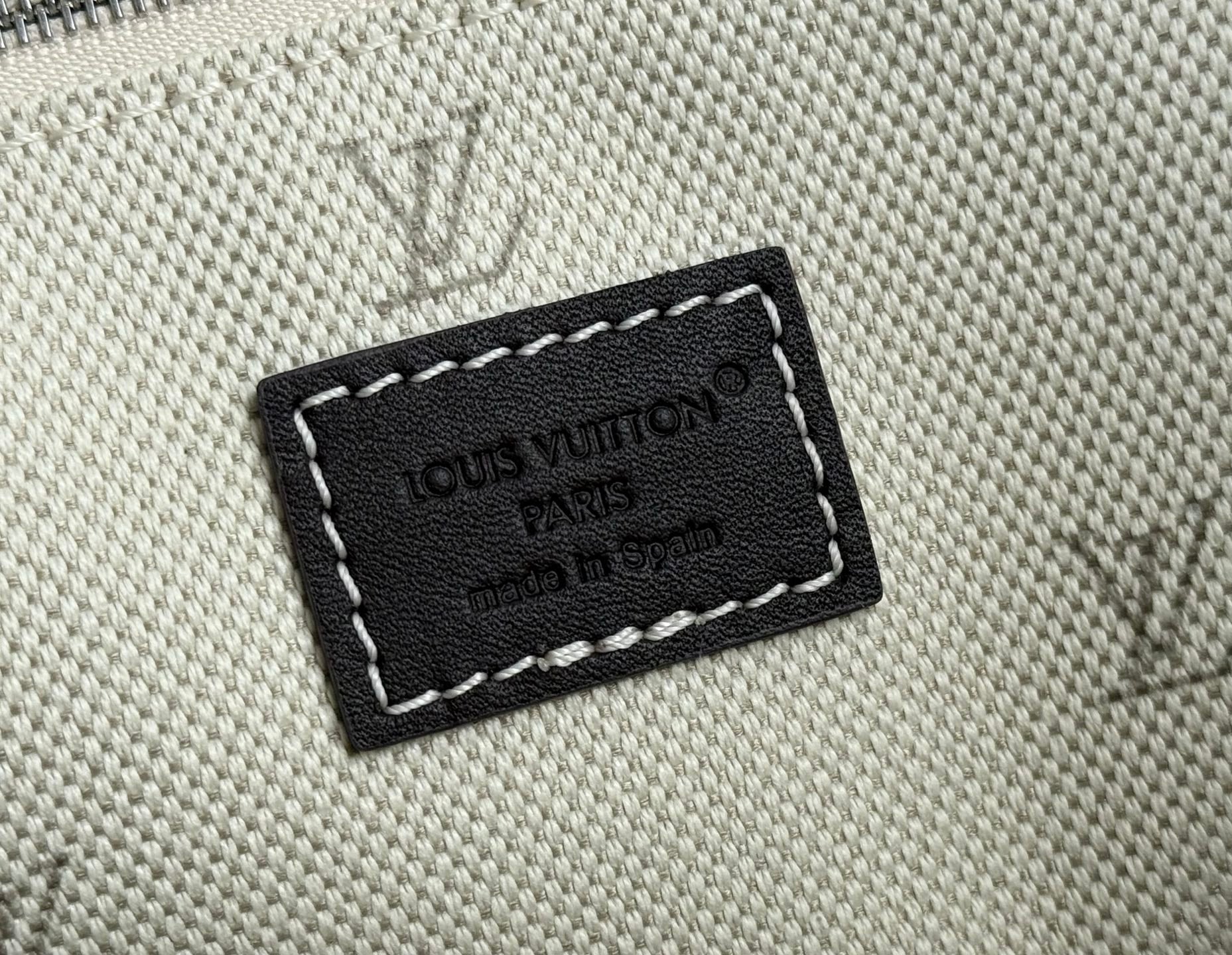 Beige textured bag with black leather logo patch and white stitching