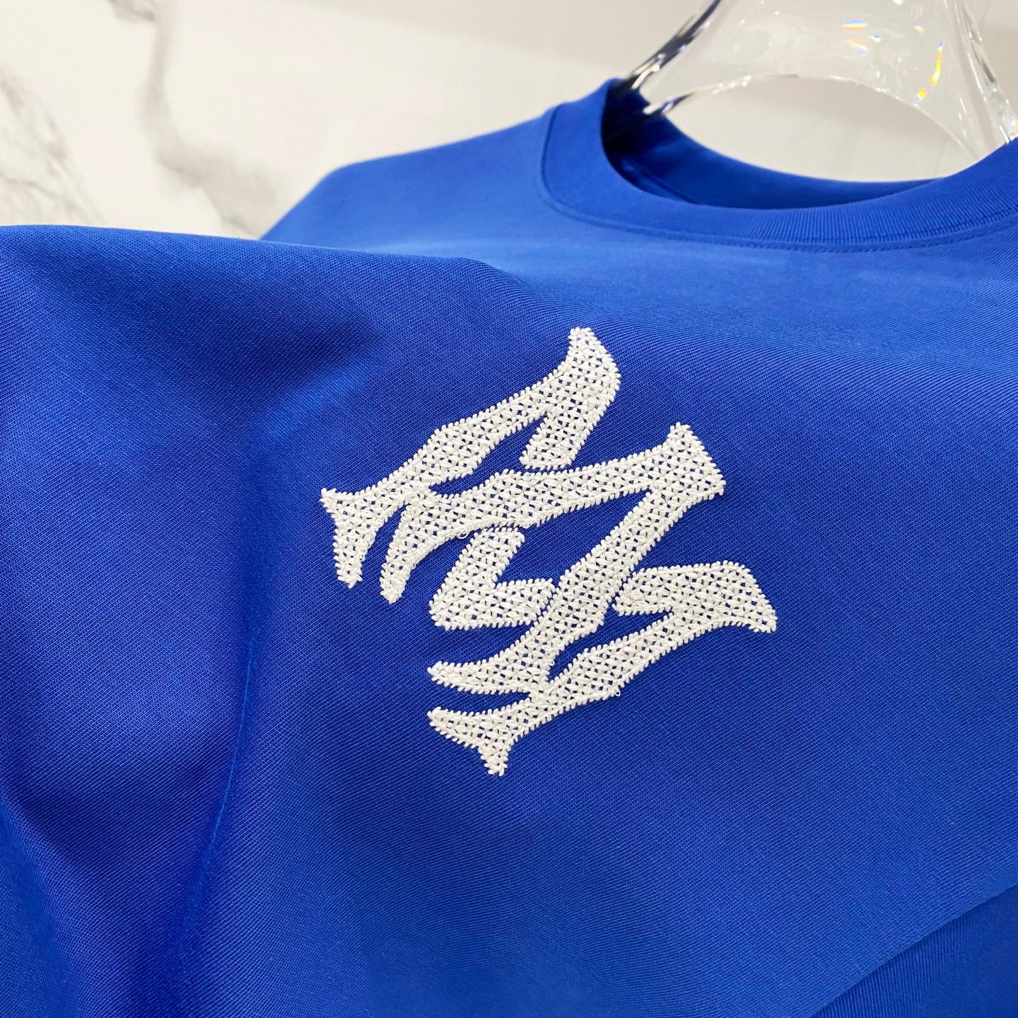 Blue T-shirt with large white monogram embroidery on the chest