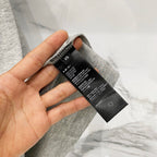 Amiri heather gray T-shirt care label close-up with hand holding tag