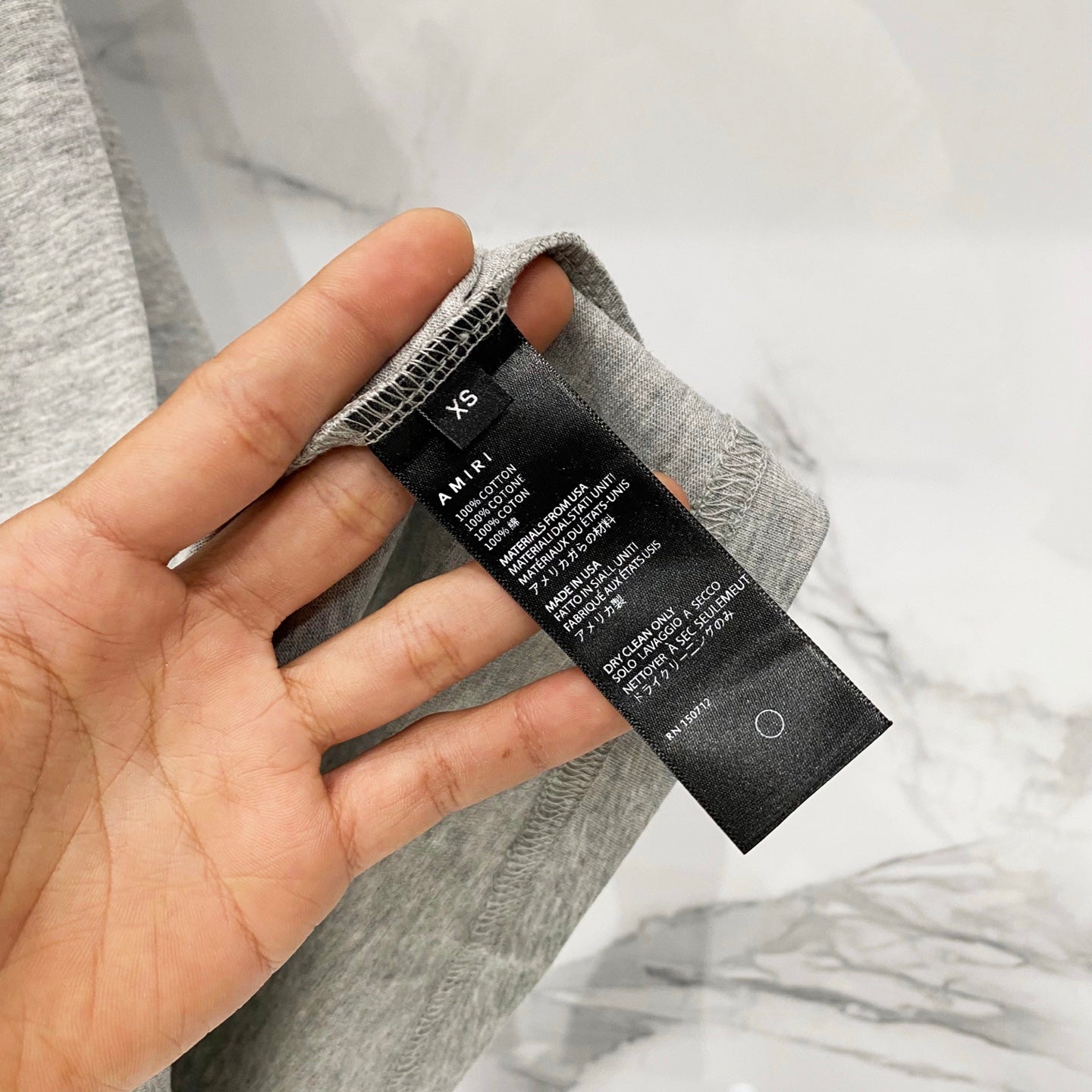 Amiri heather gray T-shirt care label close-up with hand holding tag