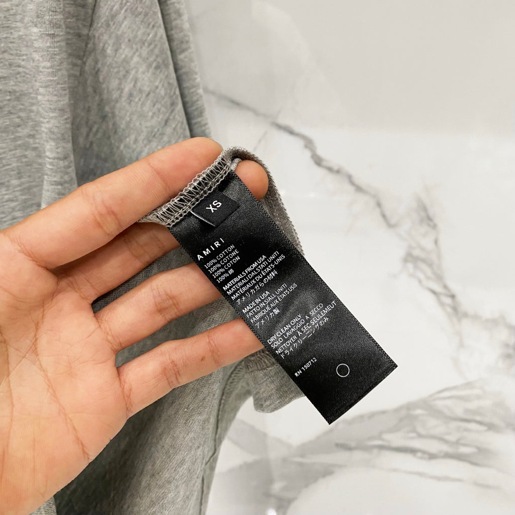 Amiri T-shirt care label at side seam on heather gray fabric