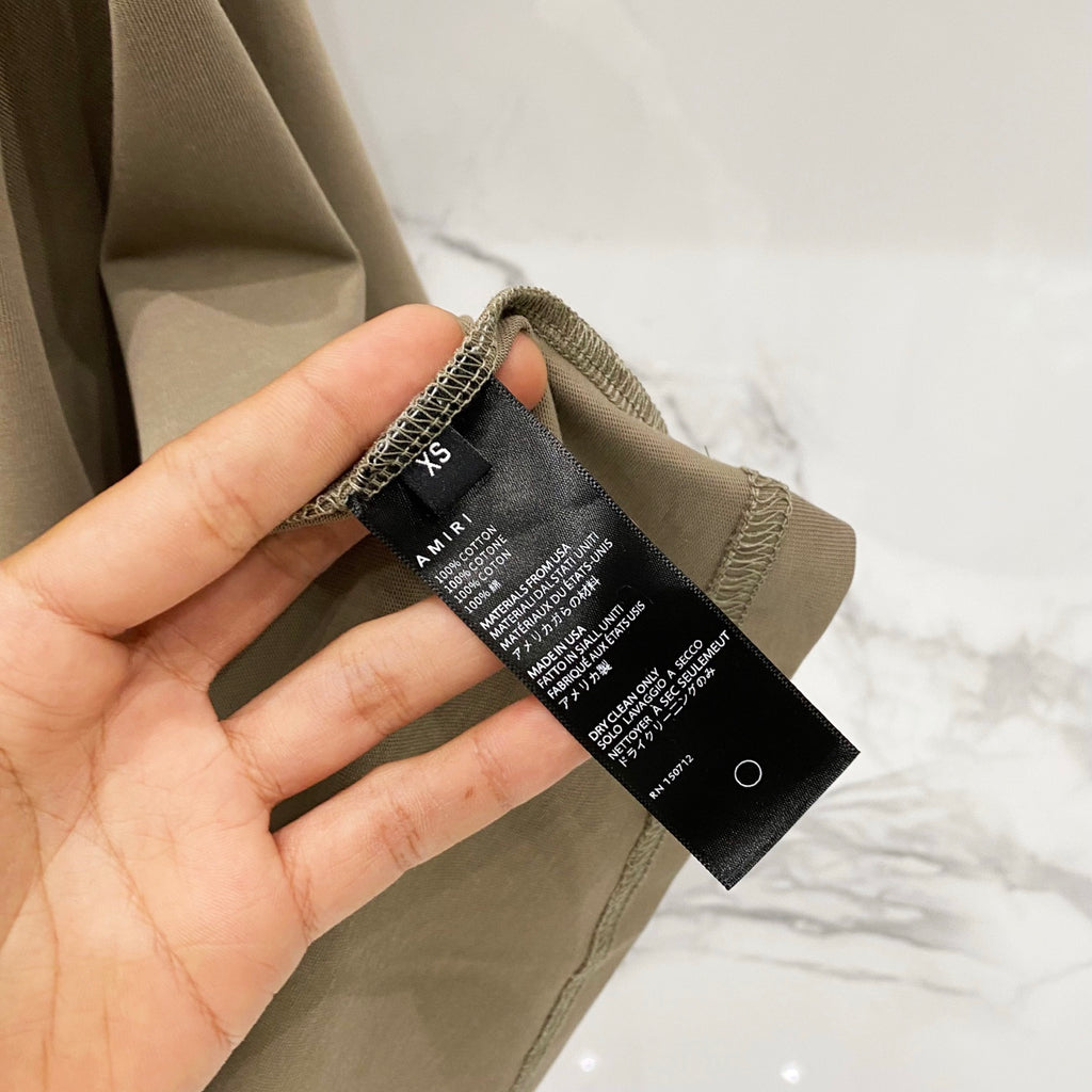 Olive T-shirt size tag on inner neck with AMIRI branding and care text