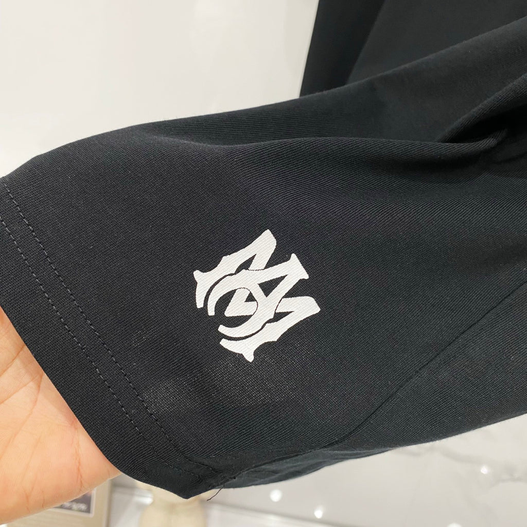 Black Amiri T-shirt sleeve with small cream emblem graphic near cuff