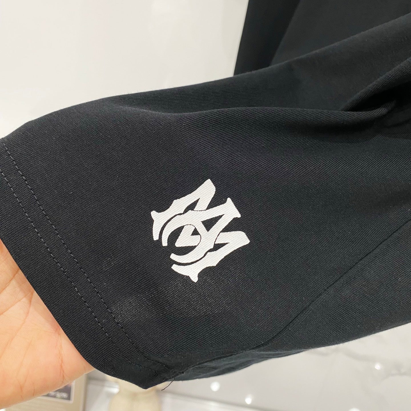 Black Amiri T-shirt sleeve with small cream emblem graphic near cuff