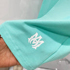 Turquoise T-shirt sleeve with small white AMIRI logo