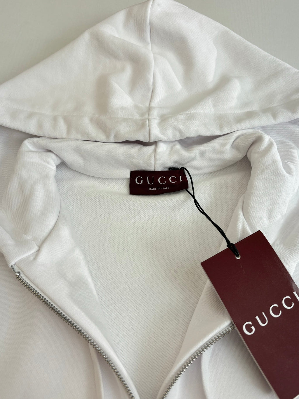 Gucci white zip hoodie with hood drawcord and zipper, close-up of hang tag