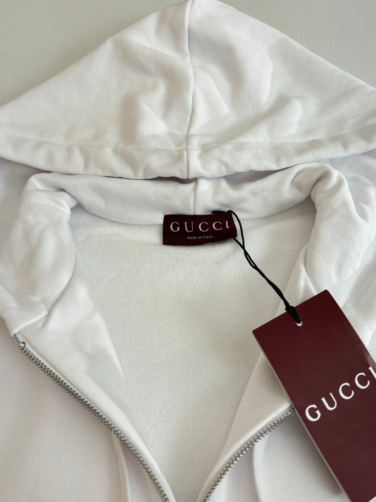 Gucci white zip hoodie with hood drawcord and zipper, close-up of hang tag