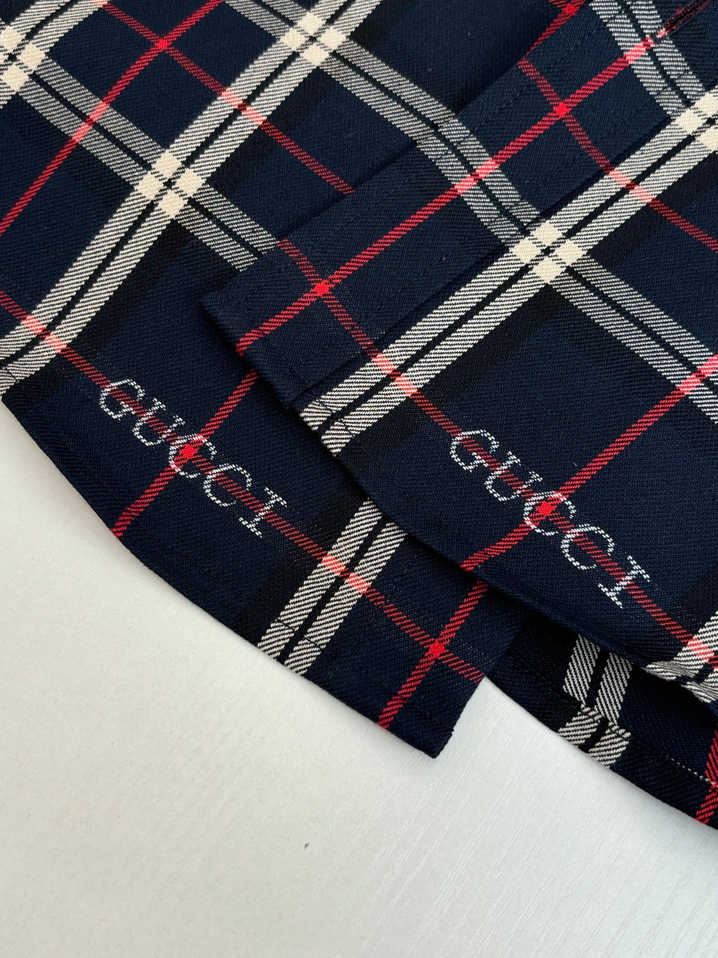 Gucci long-sleeve plaid cuff close-up, dark navy with red and white grid stripe