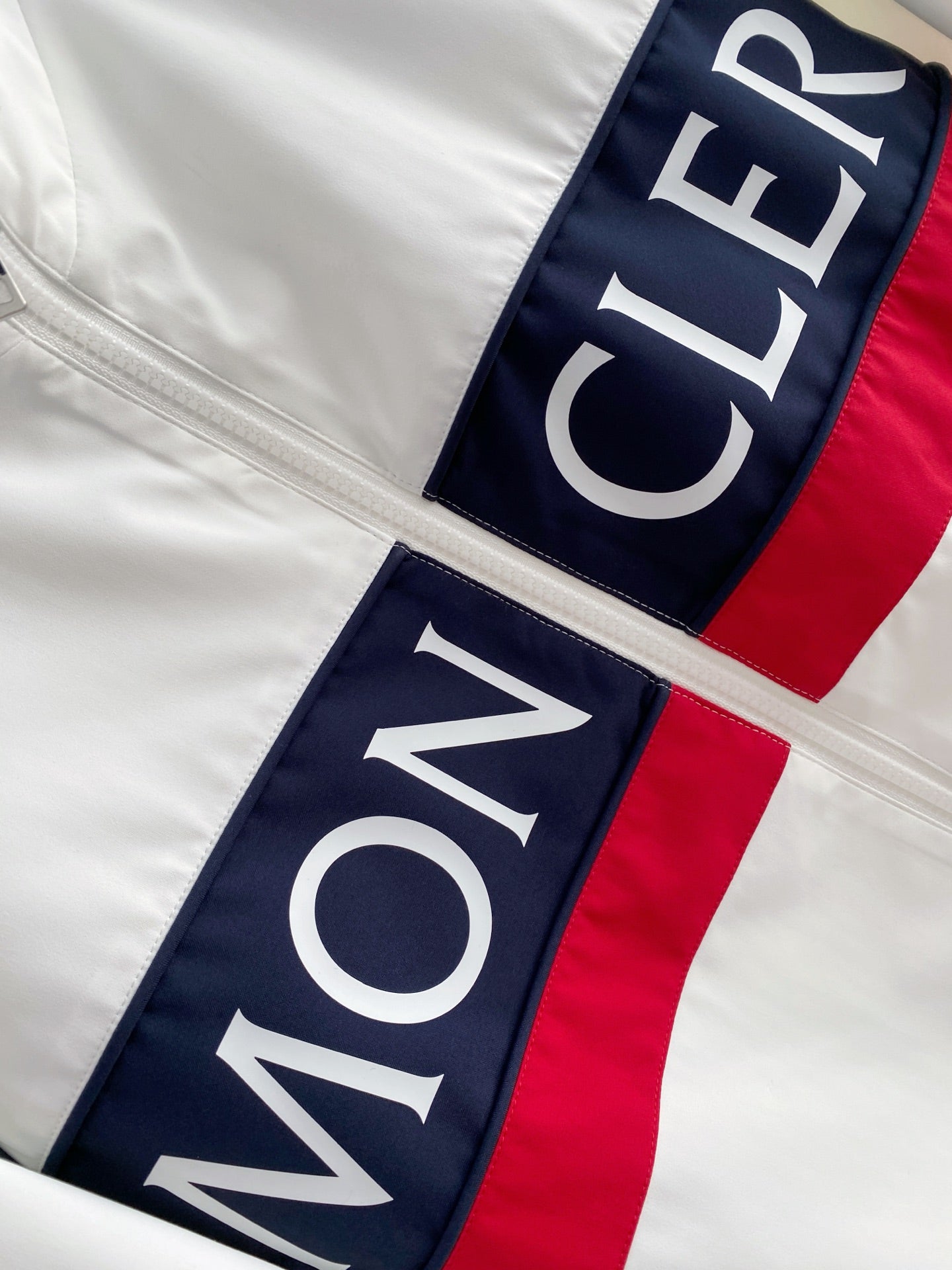 White long jacket with vertical MONCLER logo patch on navy/red trim