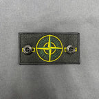 Embroidered Stone Island logo patch with yellow compass graphic on gray fabric