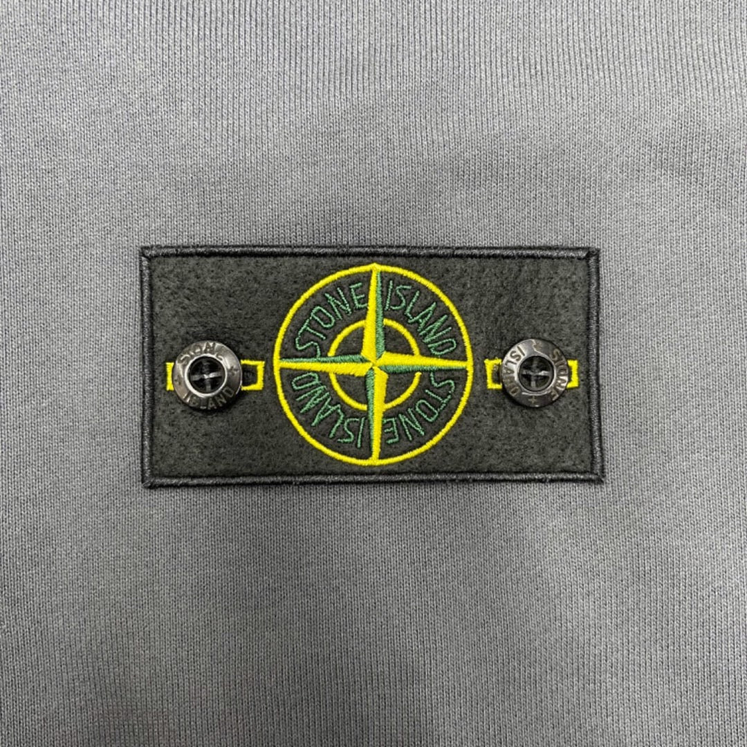 Embroidered Stone Island logo patch with yellow compass graphic on gray fabric
