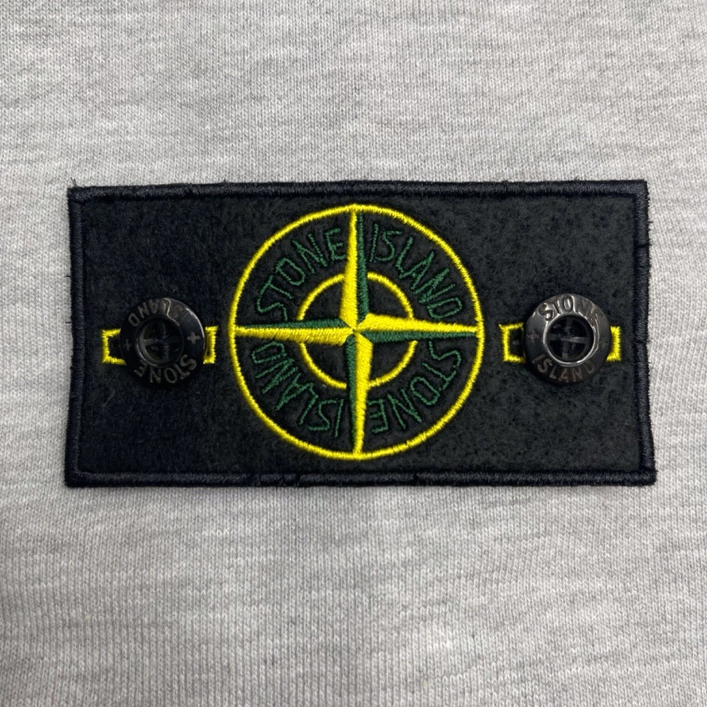 Stone Island chest patch with yellow compass graphic on light gray marl hoodie.