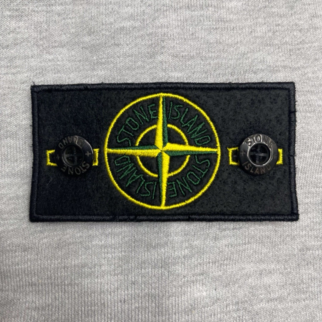 Stone Island chest patch with yellow compass graphic on light gray marl hoodie.