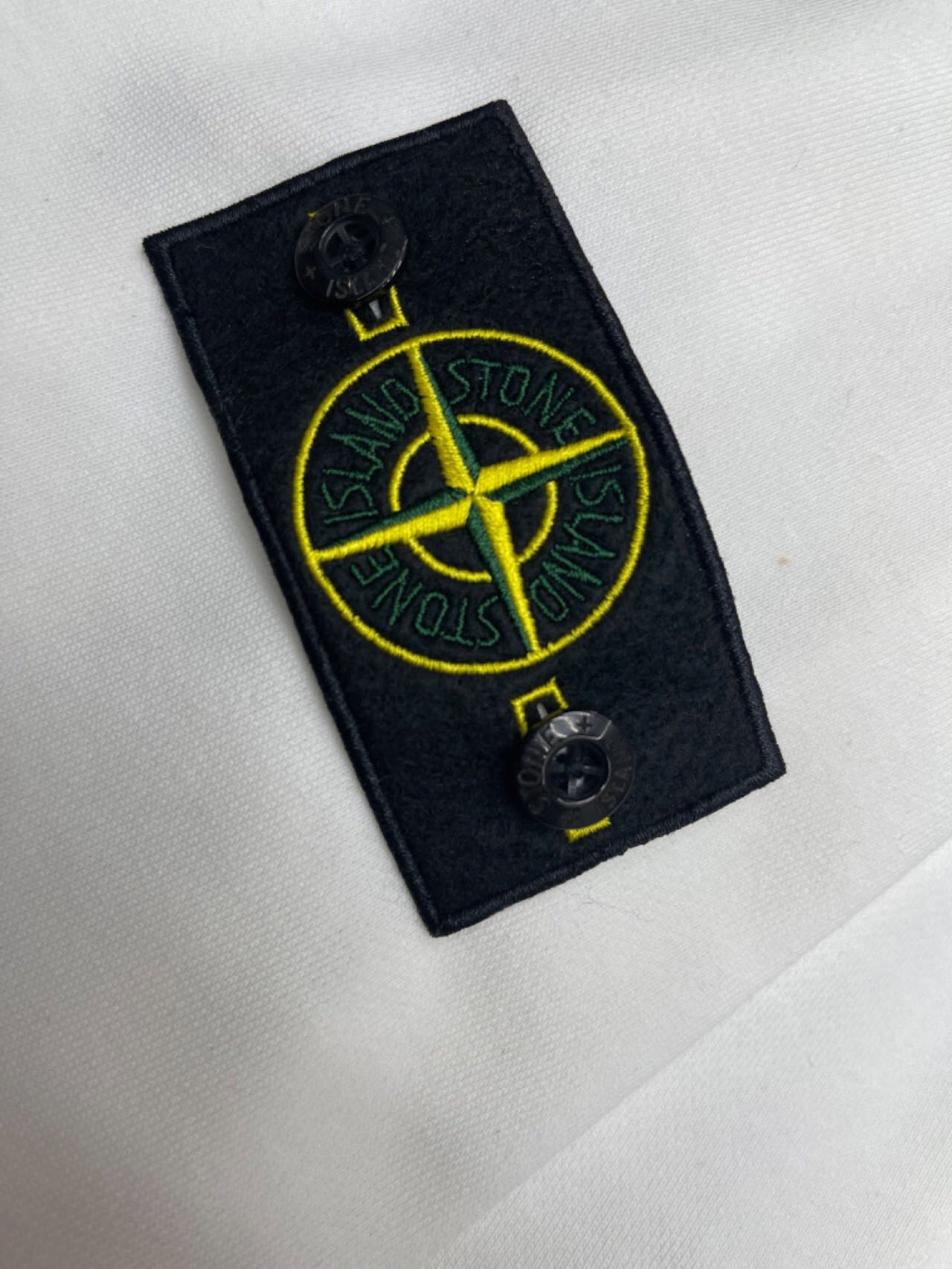 Black Stone Island logo patch with yellow compass graphic on white fabric