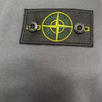Stone Island logo badge with crossed lines on gray fabric