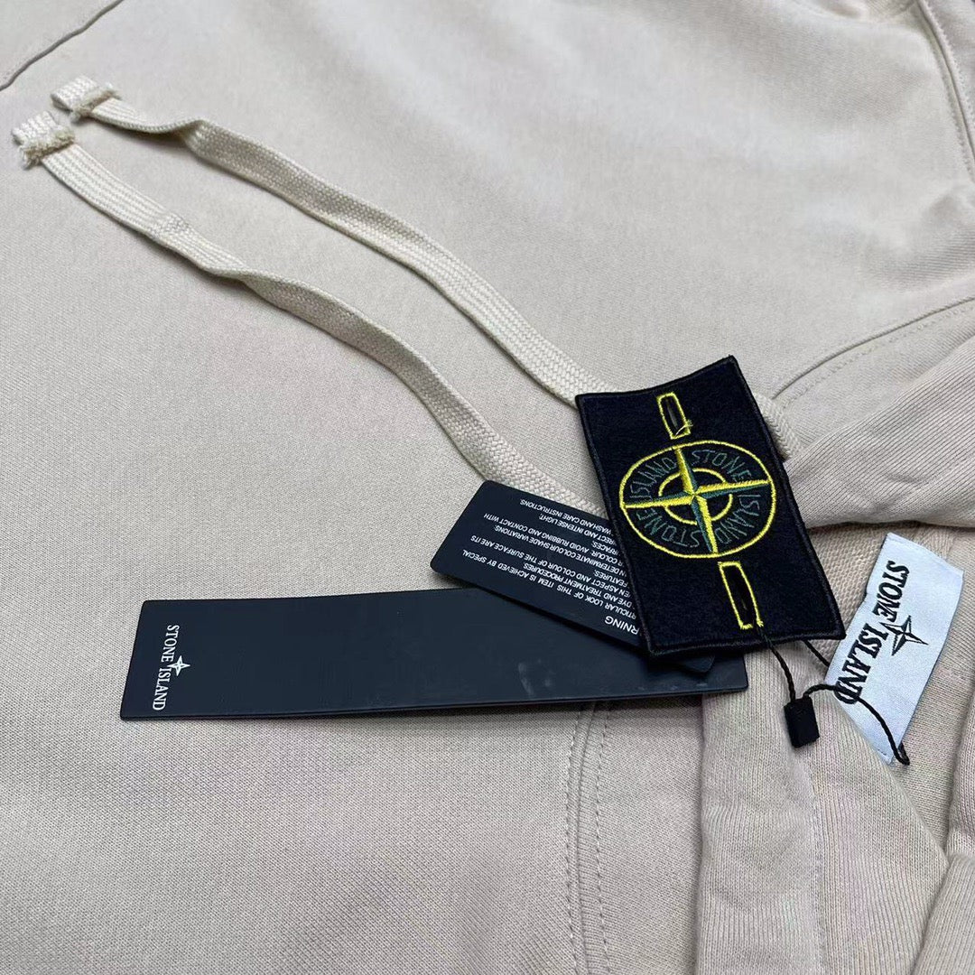 Cream hoodie chest close-up with drawstring, pocket seam, and hang tags