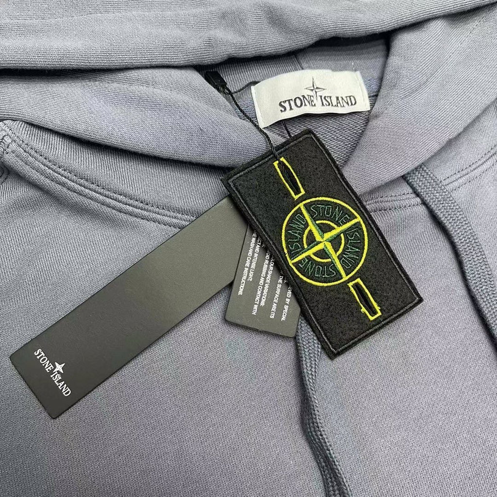 Stone Island neck label close-up with hang tags on slate blue hood