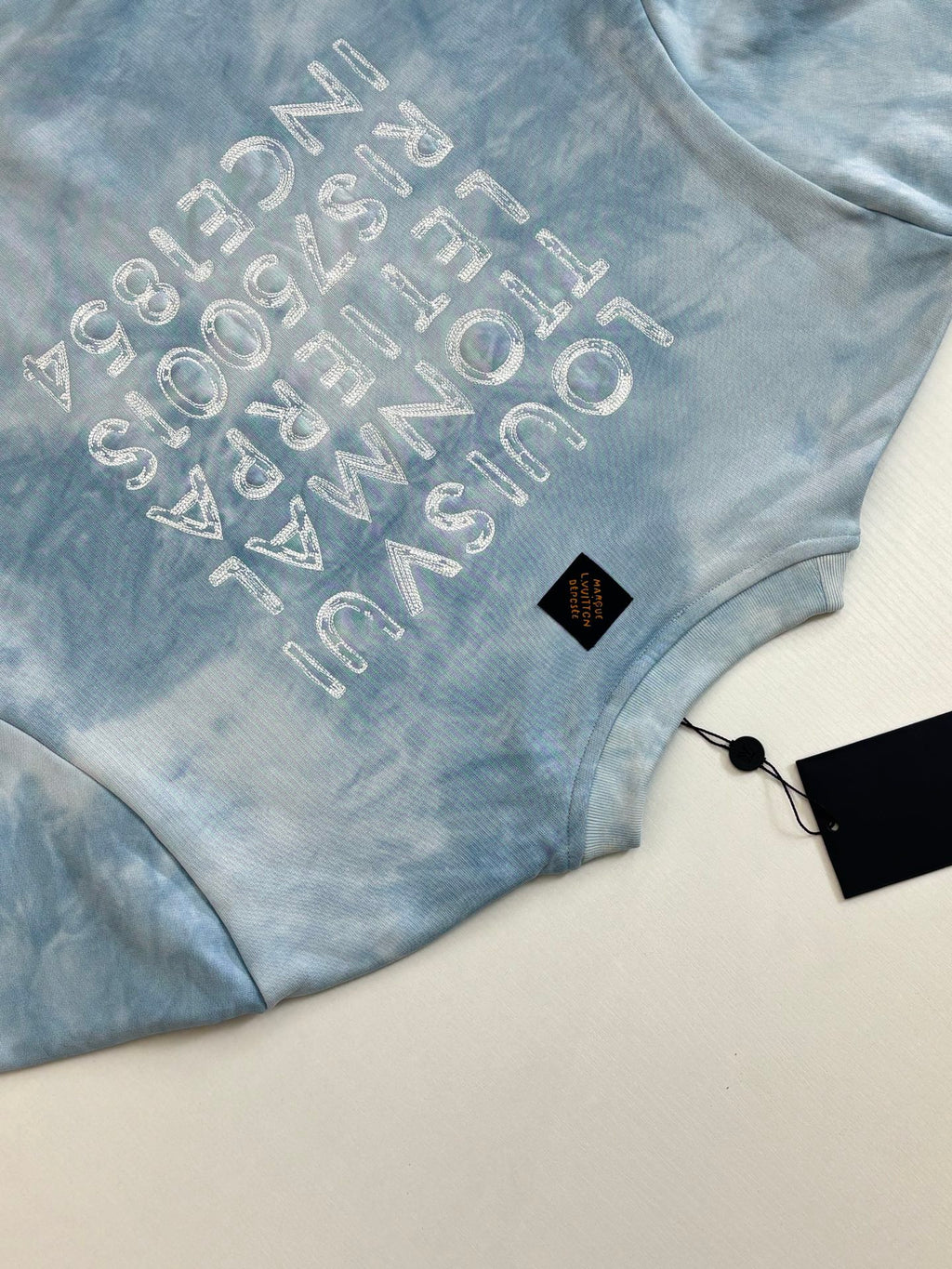 Light blue tie-dye sweatshirt with arched glitter logo text on chest
