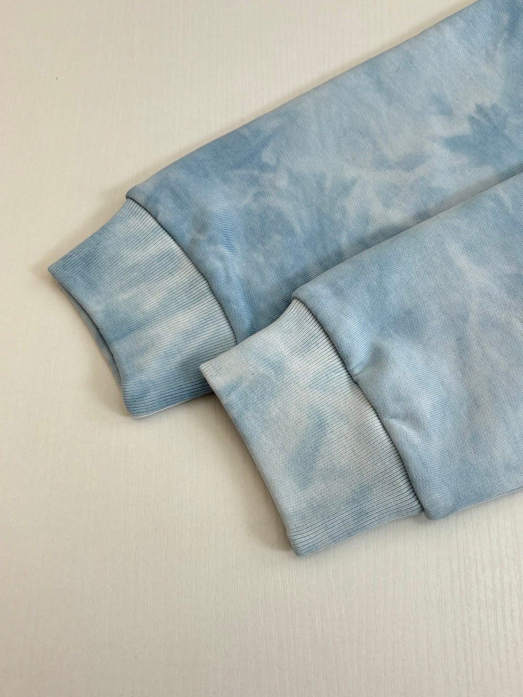 Light blue tie-dye sweatshirt laid flat with ribbed cuffs