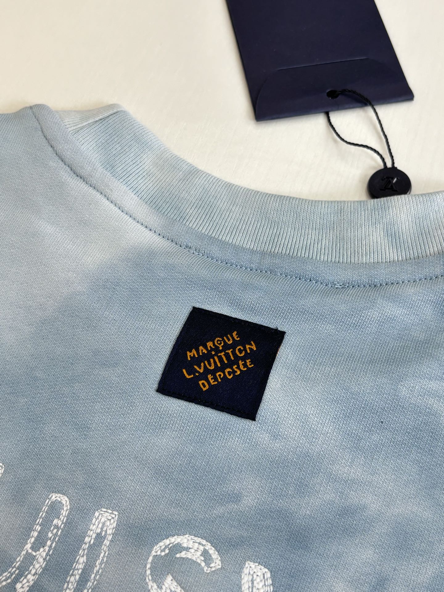 Light blue crewneck sweatshirt with small black logo tag near neckline