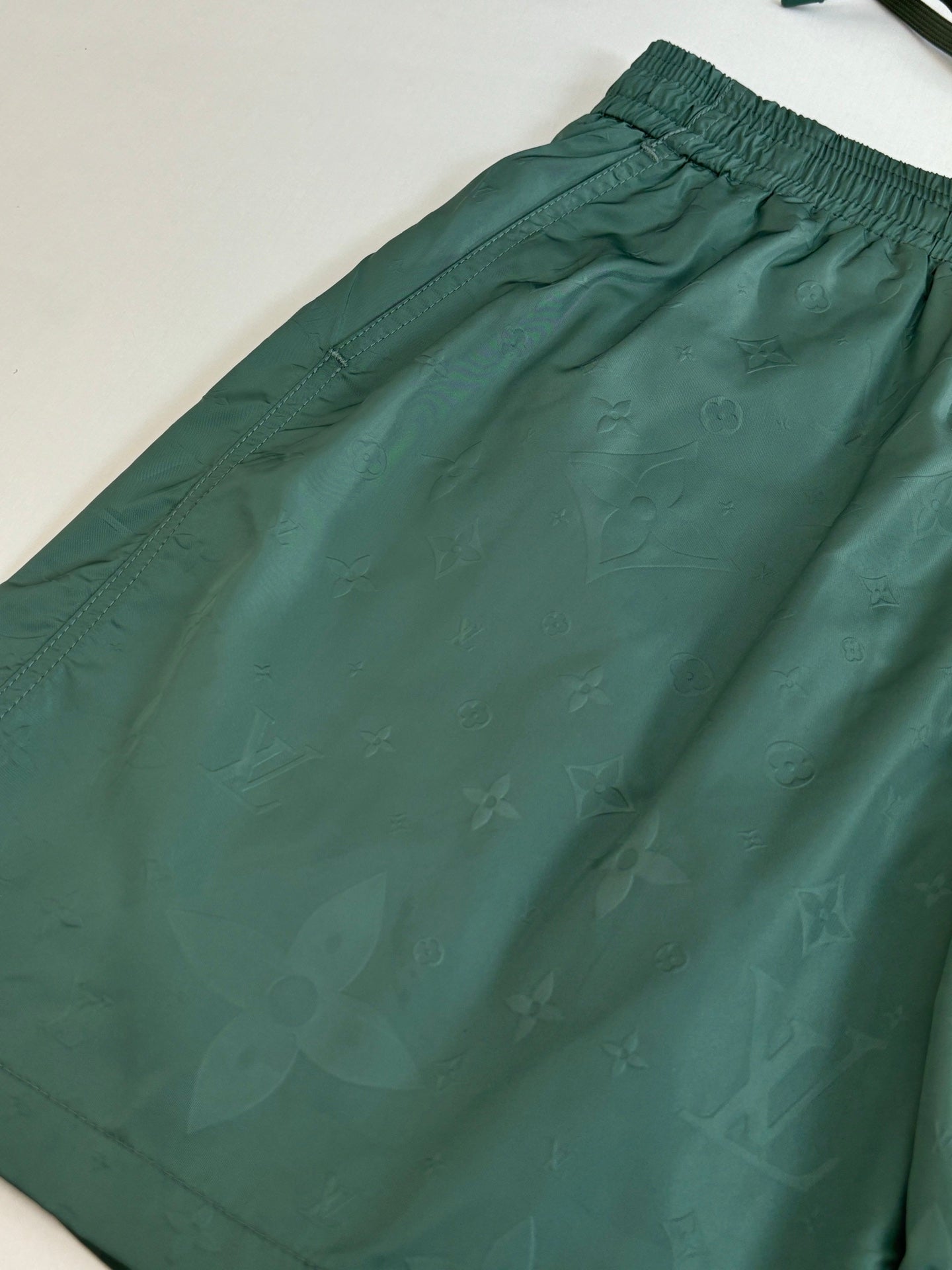 Green Louis Vuitton shorts fabric close-up with subtle monogram pattern.