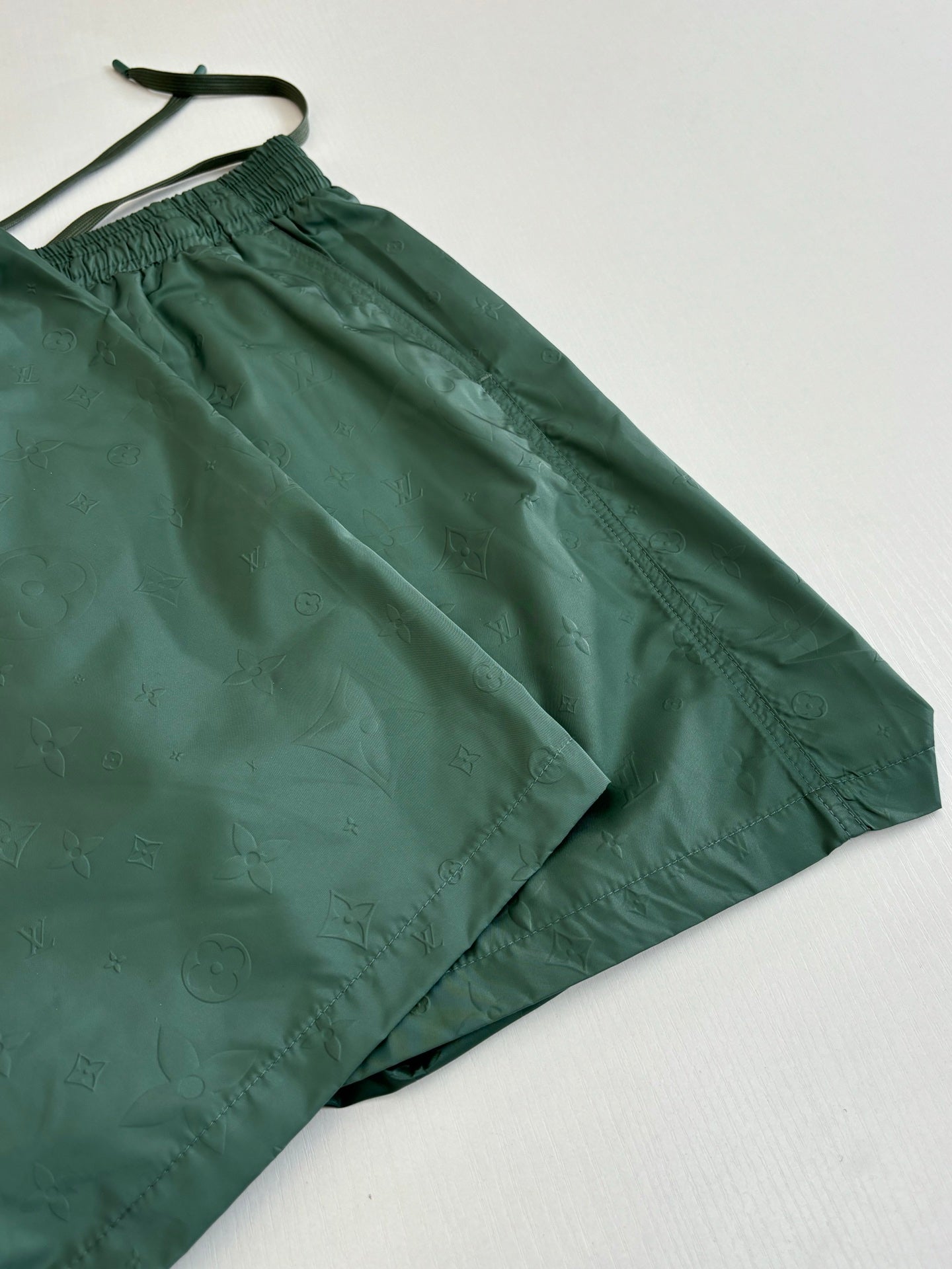 Green Louis Vuitton shorts laid out, with drawstring and elastic waistband.