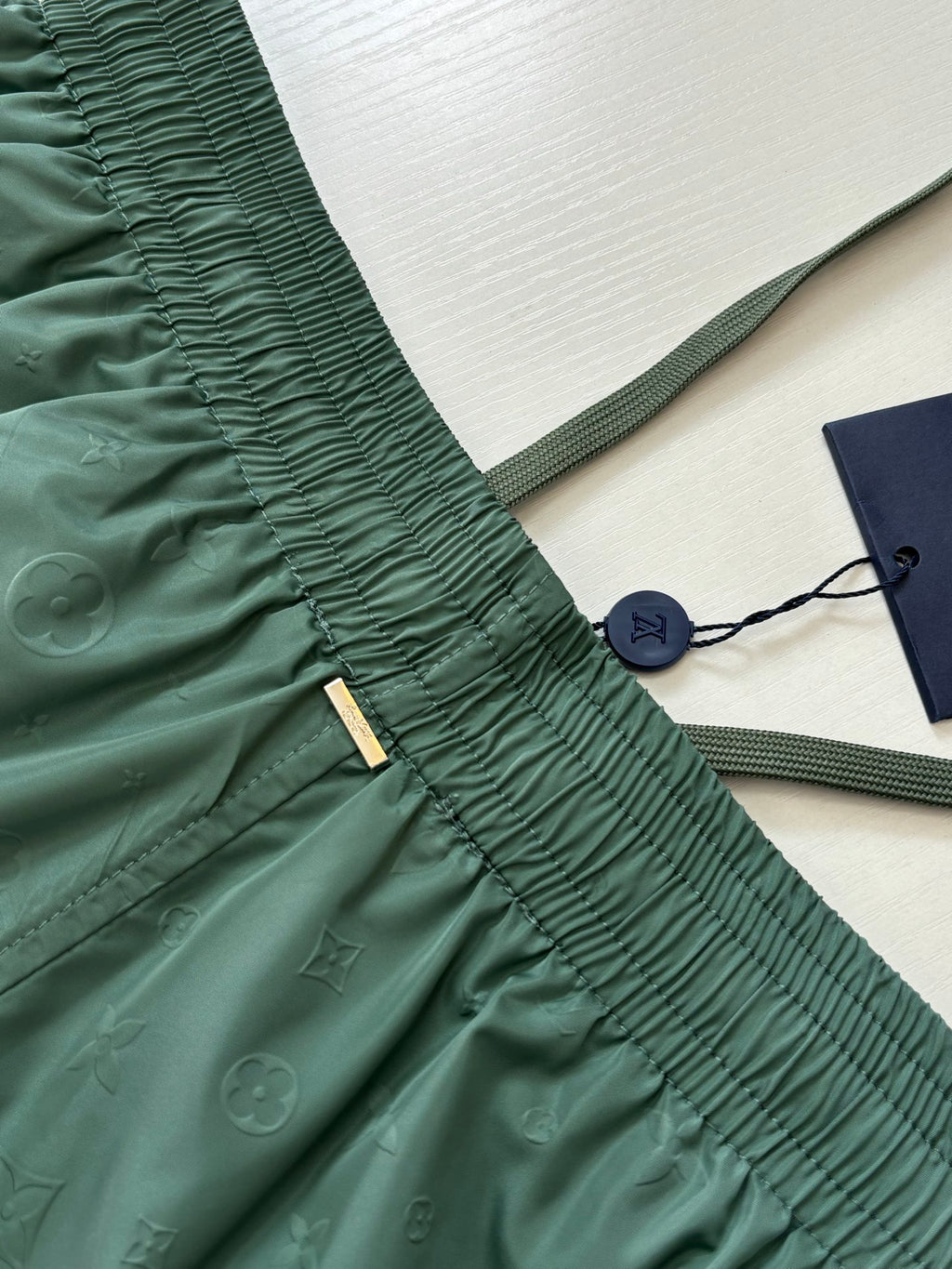 Green Louis Vuitton shorts waistband close-up with gold brand tag and drawcord.