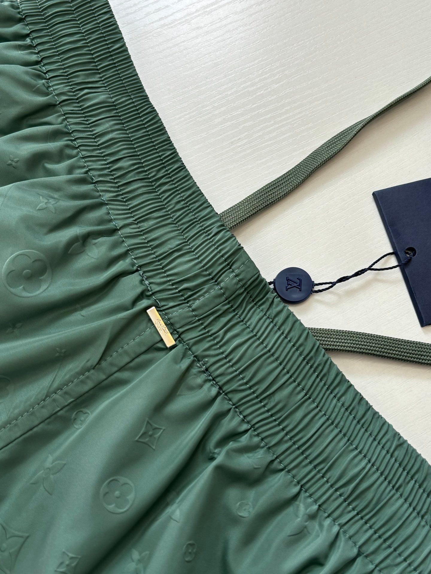 Green Louis Vuitton shorts waistband close-up with gold brand tag and drawcord.