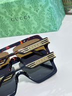 Gucci sunglasses detail, black frame with gold Gucci logo and dark lenses