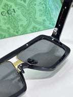 Gucci sunglasses close-up with black frame, gold hinge hardware, and dark lenses
