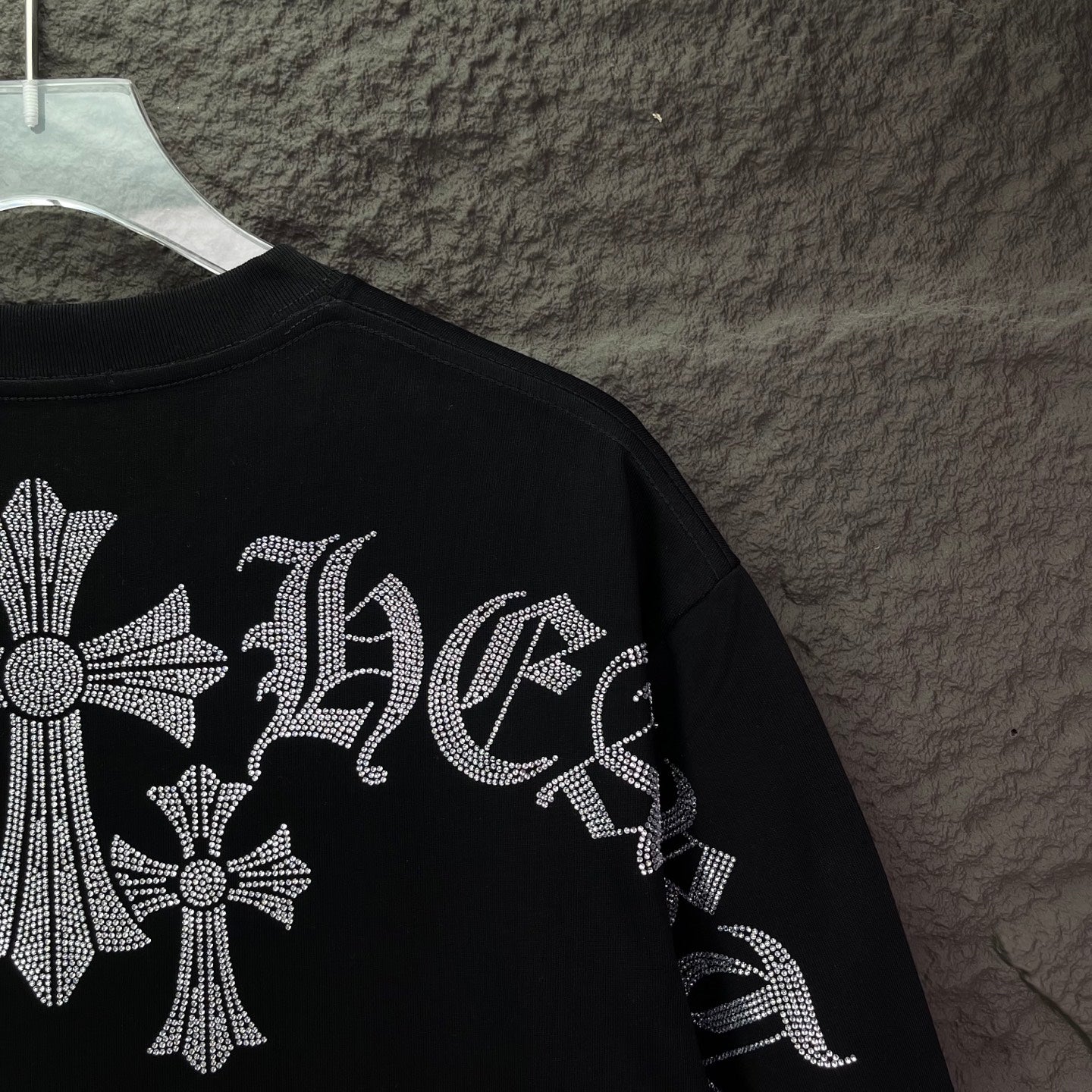 Black T-shirt sleeve detail with rhinestone cross and patterned lettering