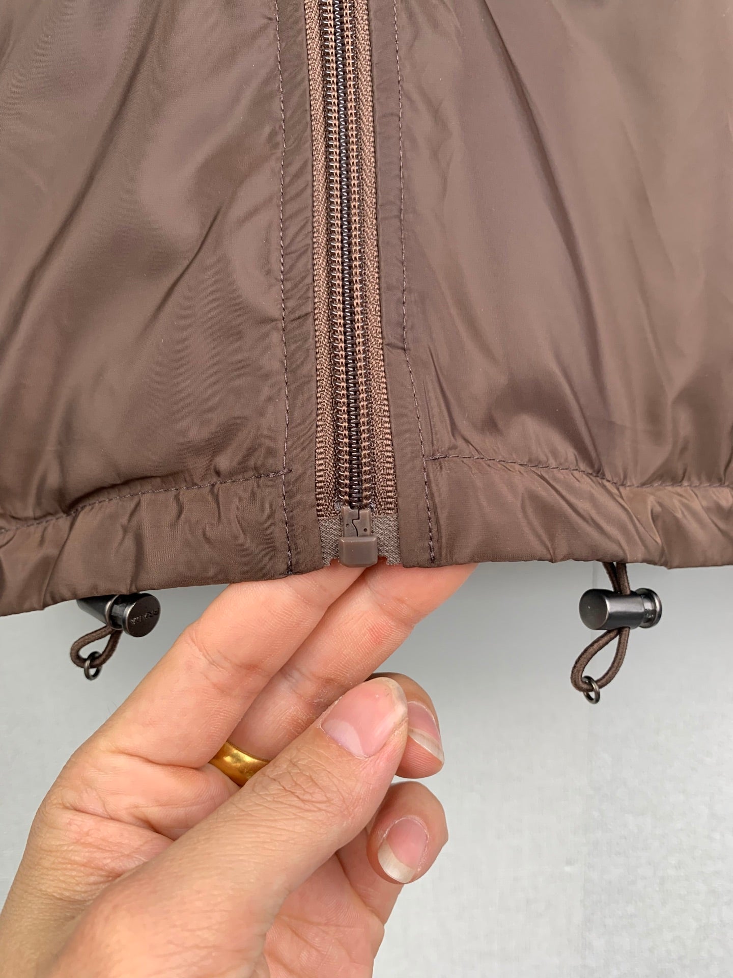 Brown jacket hem close-up with zipper and metal drawcord eyelets