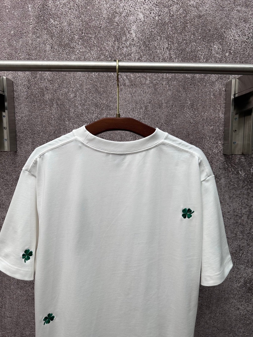 White back of T-shirt with green clover embroidery near hem and sleeves