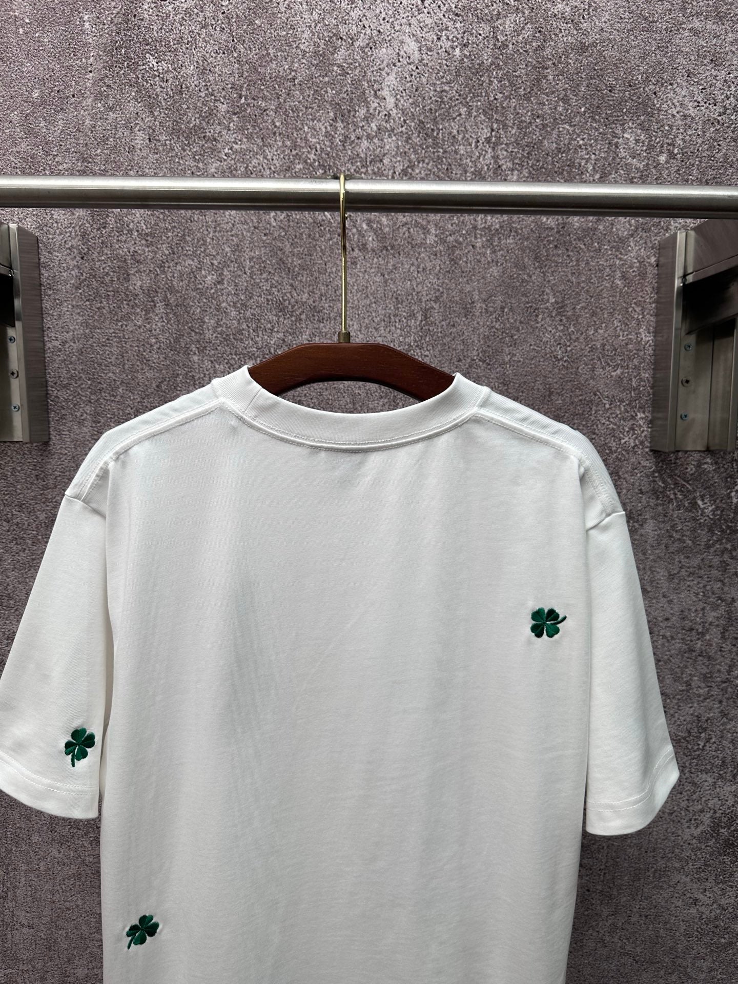 White back of T-shirt with green clover embroidery near hem and sleeves