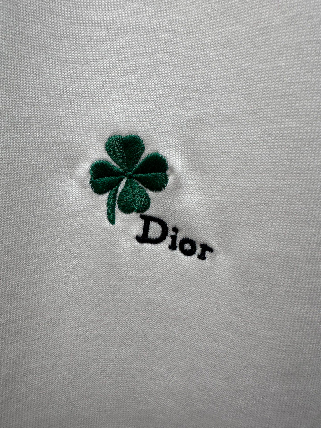 Green four-leaf clover and black Dior logo embroidery on white fabric