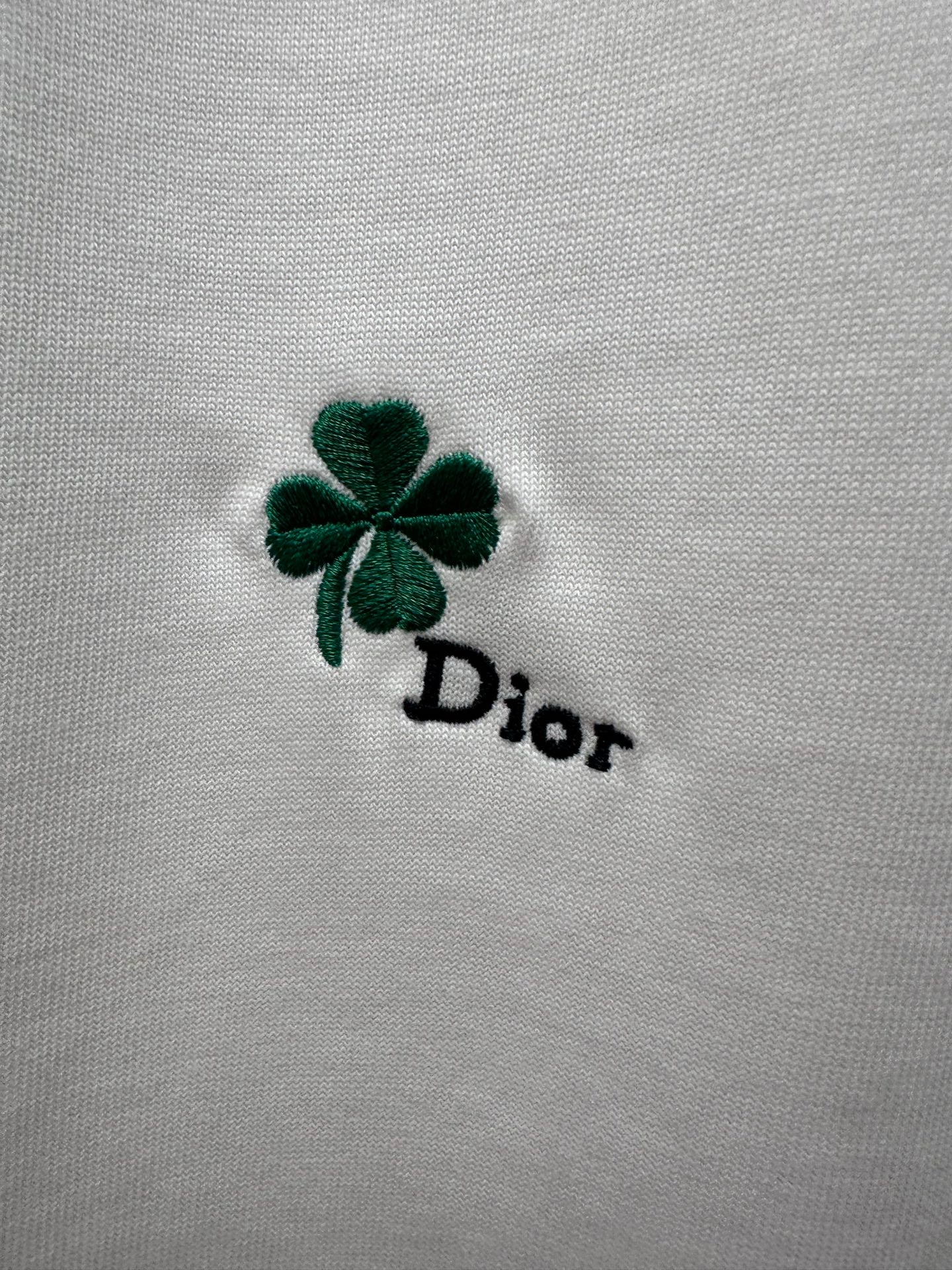 Green four-leaf clover and black Dior logo embroidery on white fabric
