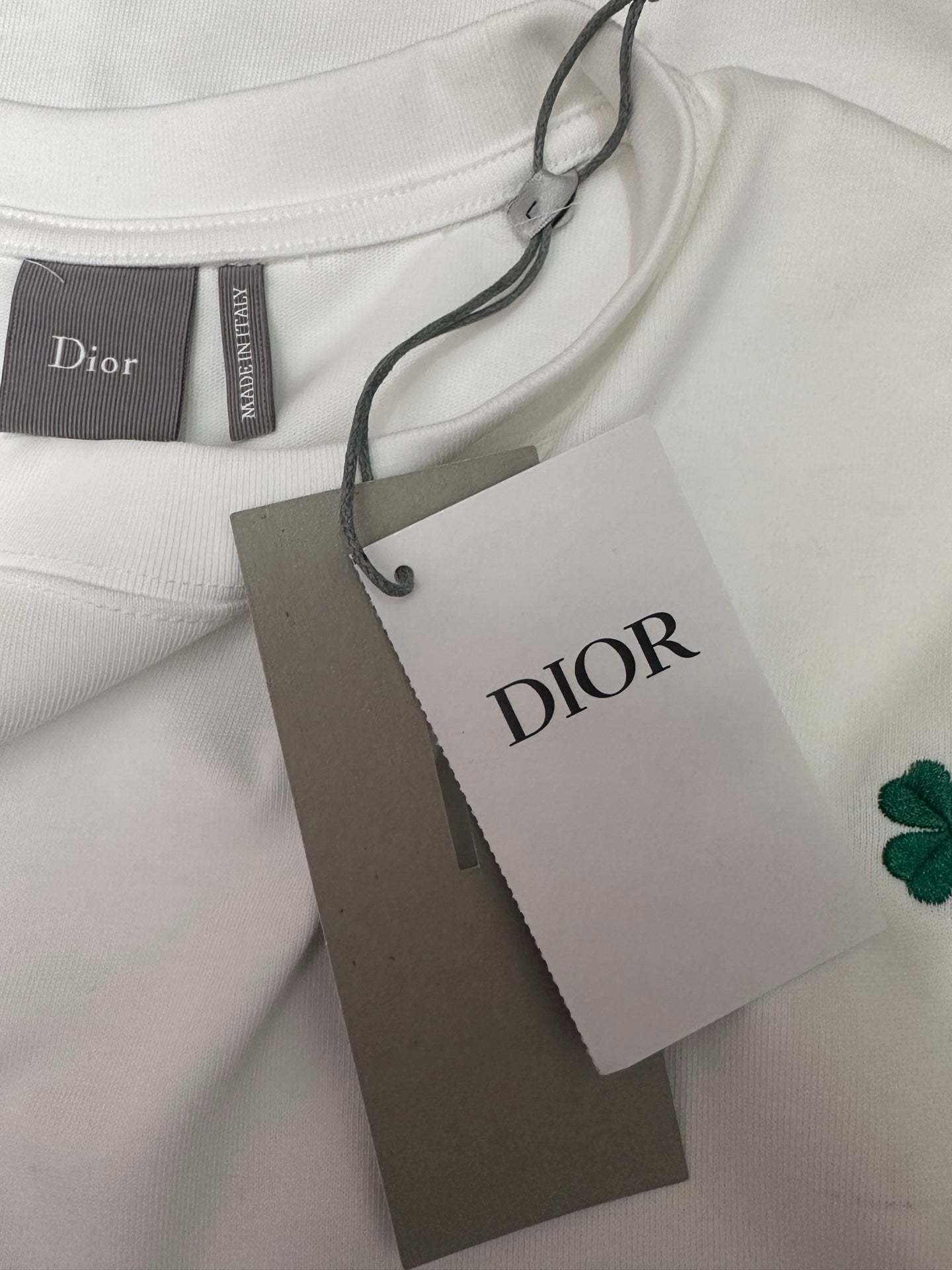 White T-shirt with Dior tag and green clover patch on fabric neckline