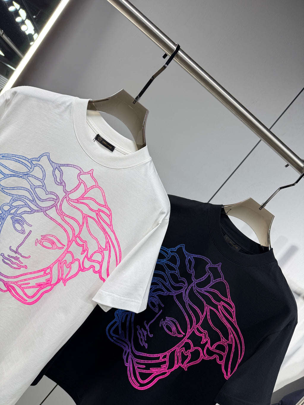 White and black Versace T-shirts on hangers with neon Medusa outline front prints