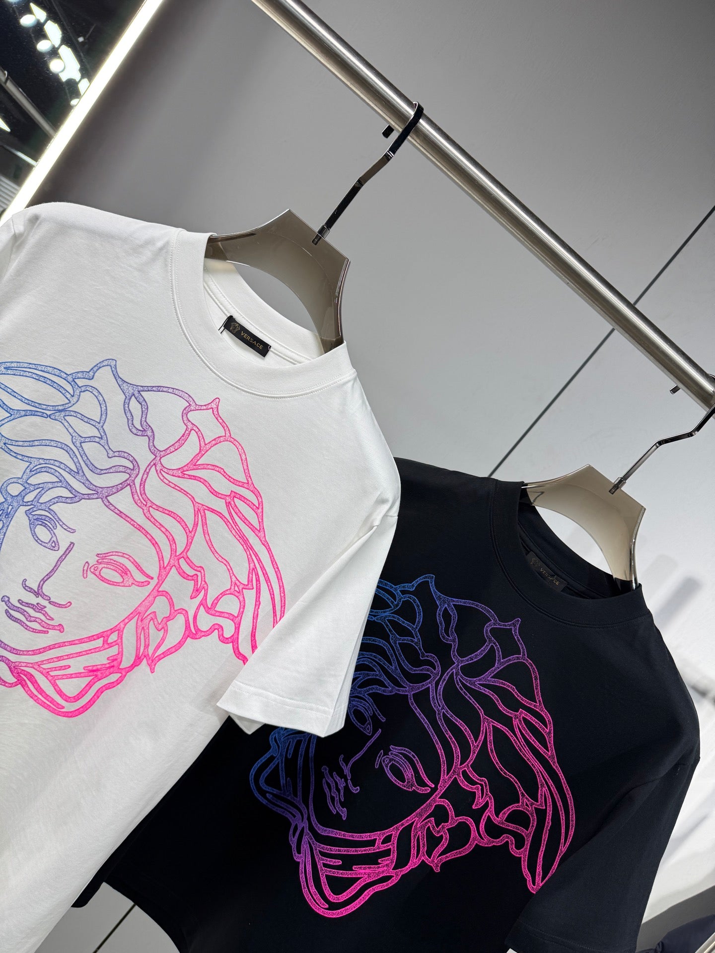 White and black Versace T-shirts on hangers with neon Medusa outline front prints