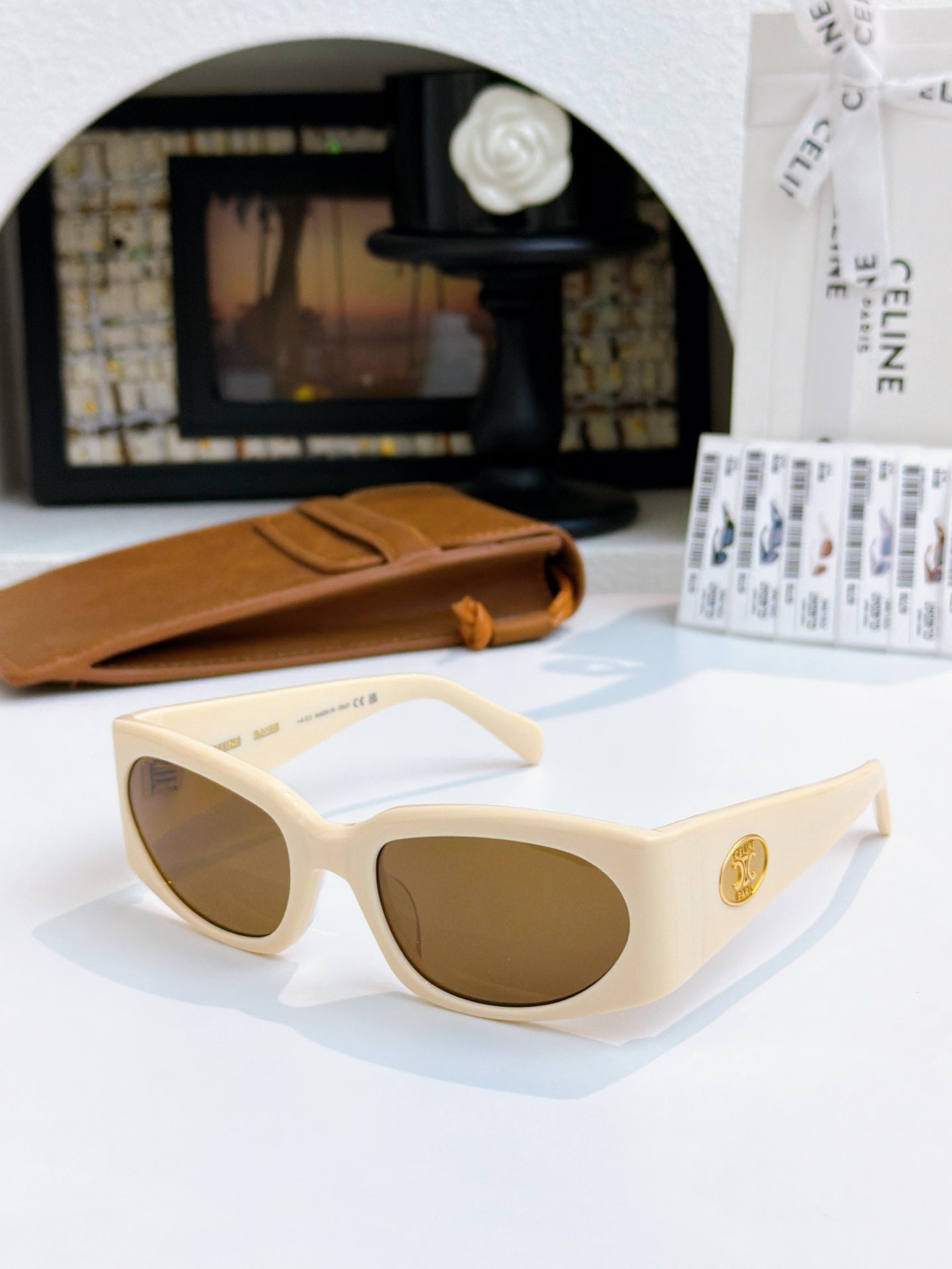 Cream cat-eye sunglasses with brown-tinted lenses and gold-tone side emblem.