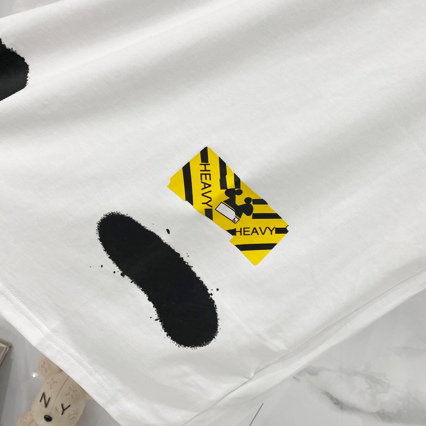 White T-shirt fabric with black “I” graphic and yellow “HEAVY” tag label