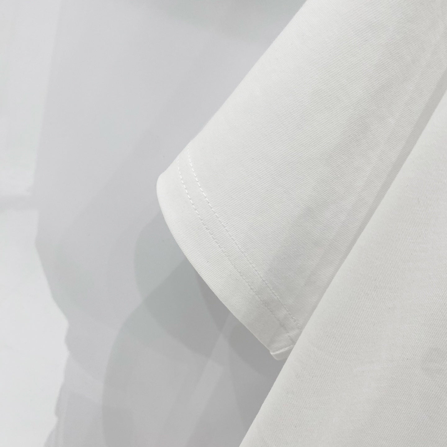 Off-white t-shirt sleeve and hem close-up with visible stitching.