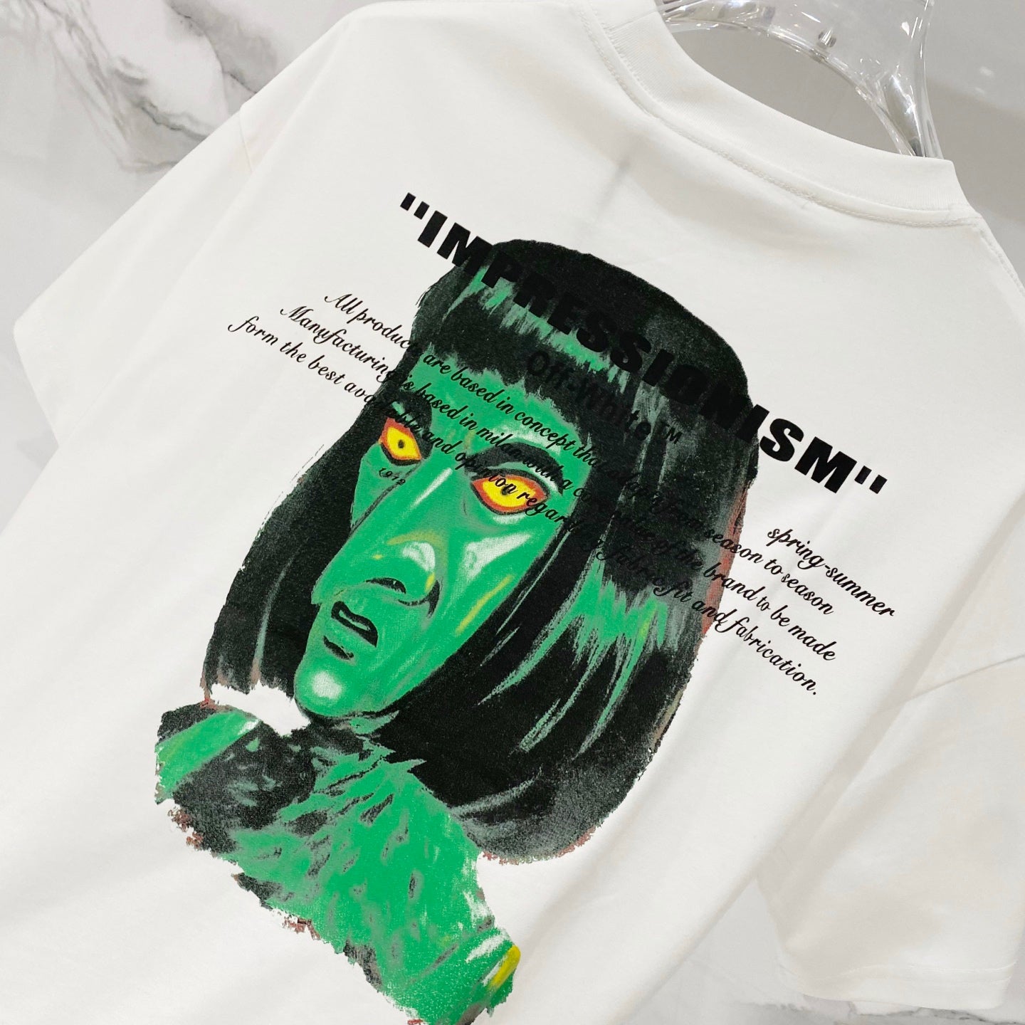 Off-white T-shirt with large green-and-black face graphic and quote-style text