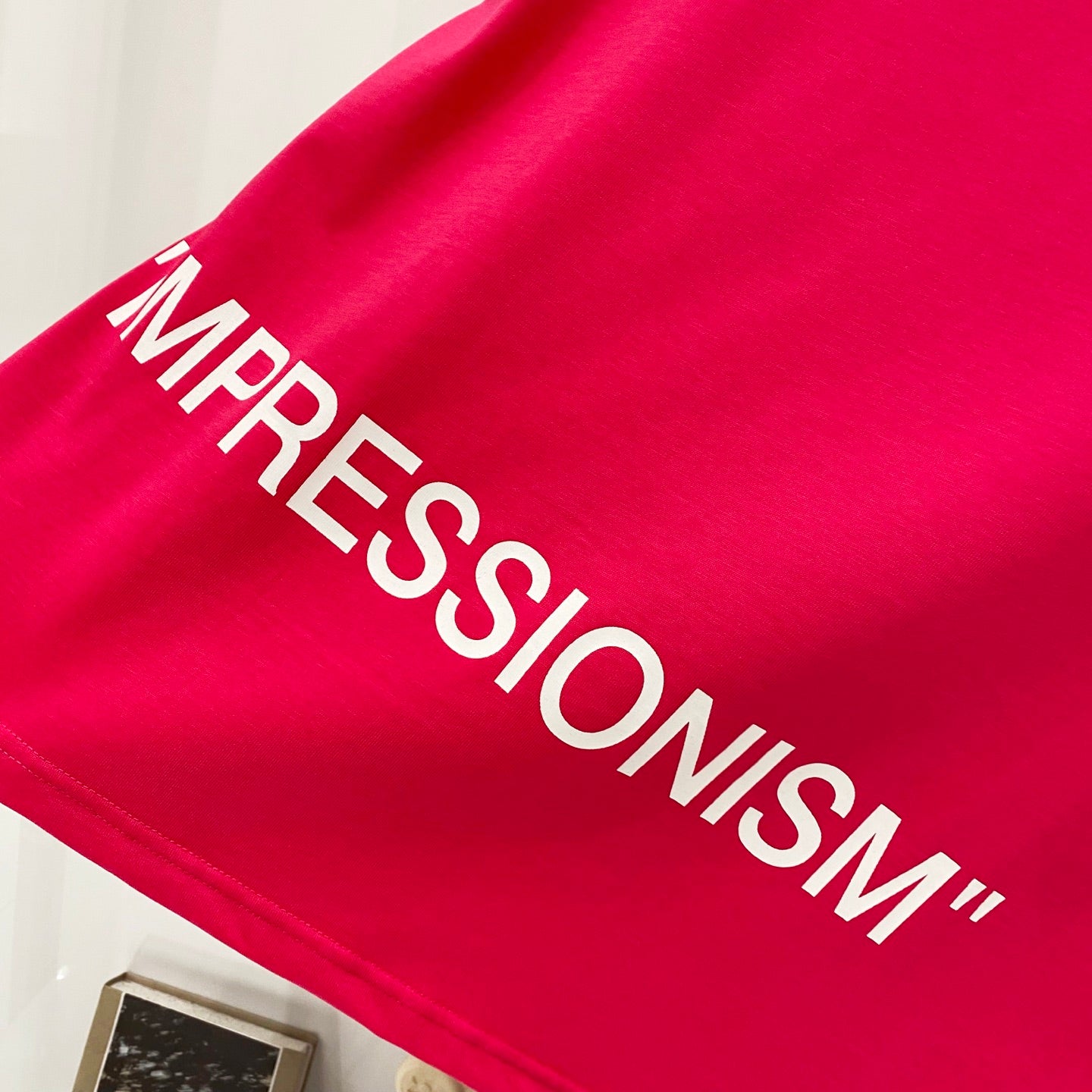 Off White red T-shirt close-up of “IMPRESSIONISM” text print across fabric.
