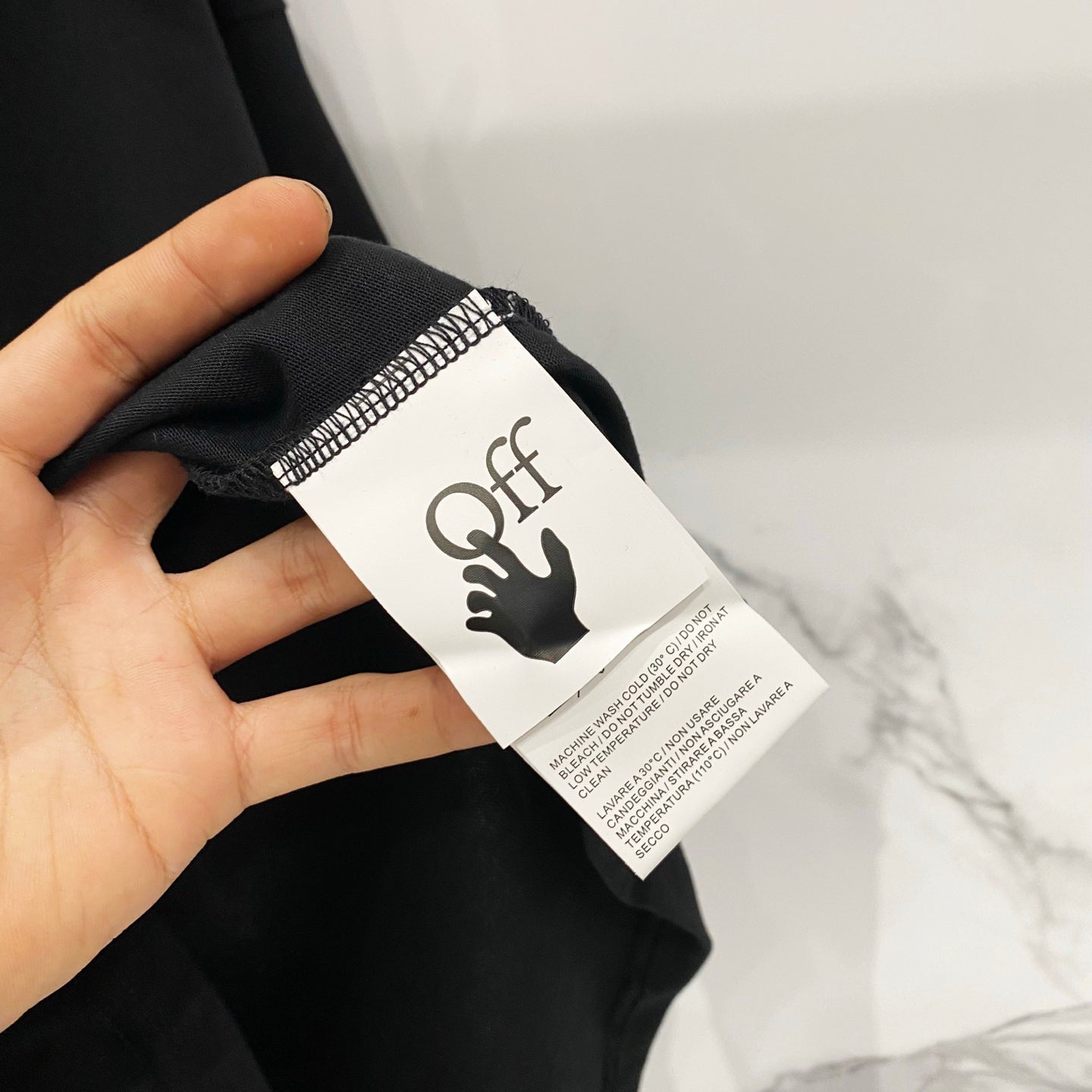 Off-White T-shirt size label close-up, black fabric with OFF tag held in hand