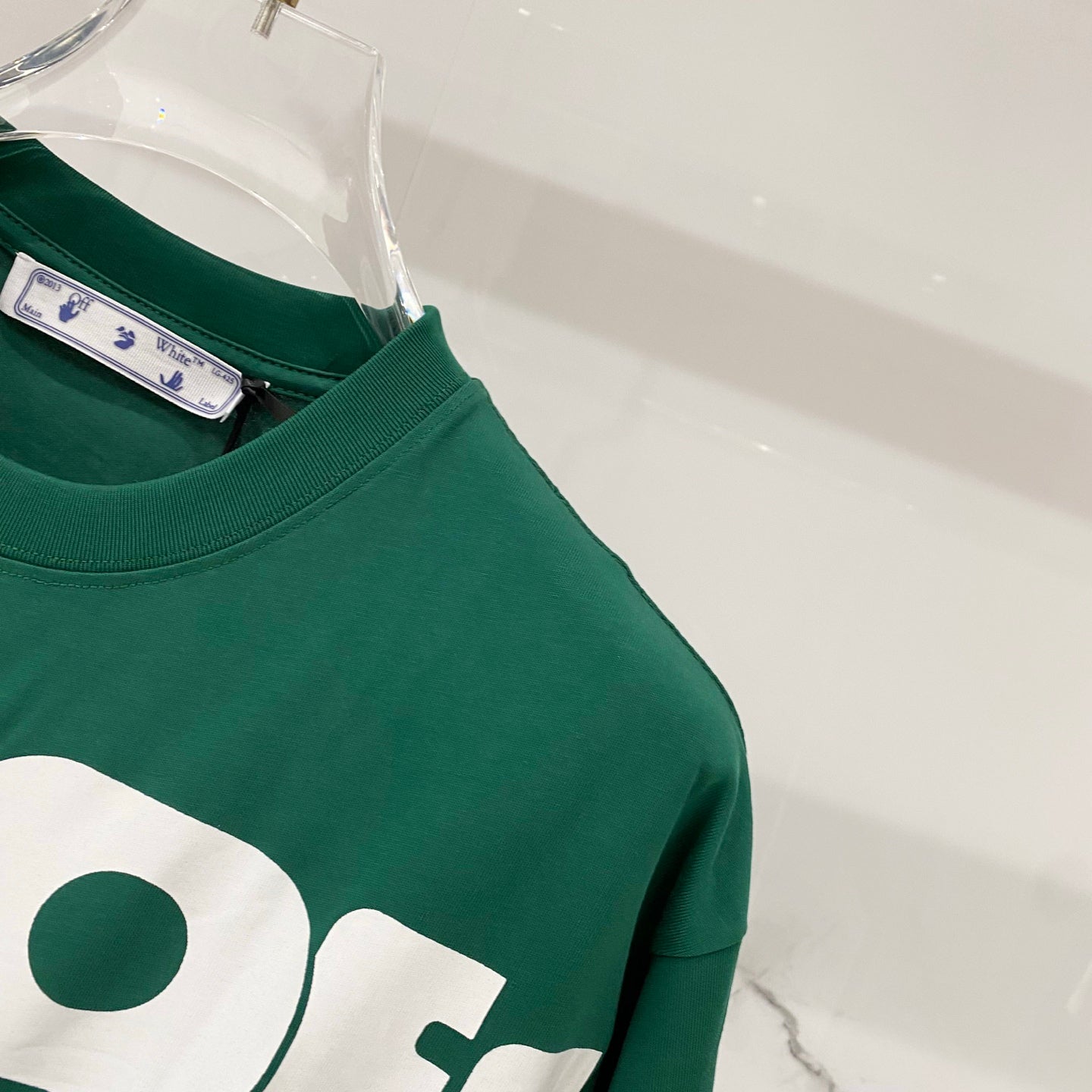 Off-White T-shirt shoulder close-up, dark green with partial white logo graphic.