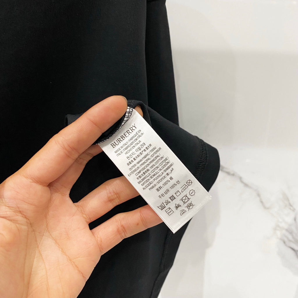 Black T-shirt fabric with Burberry care label held in hand