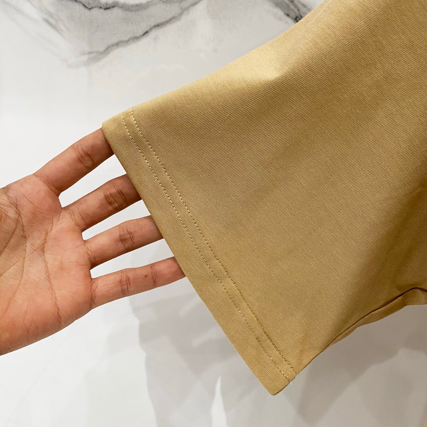Tan T-shirt sleeve hem close-up showing stitching