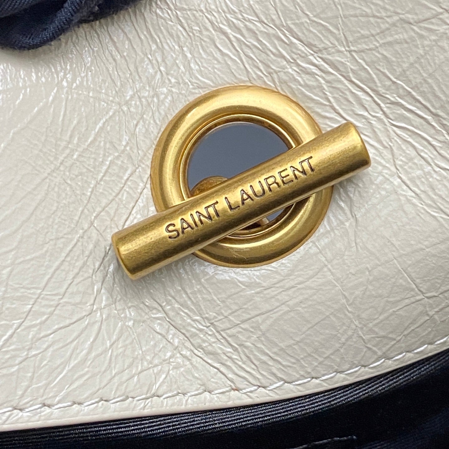 Gold clasp hardware engraved with SAINT LAUREN T on white leather