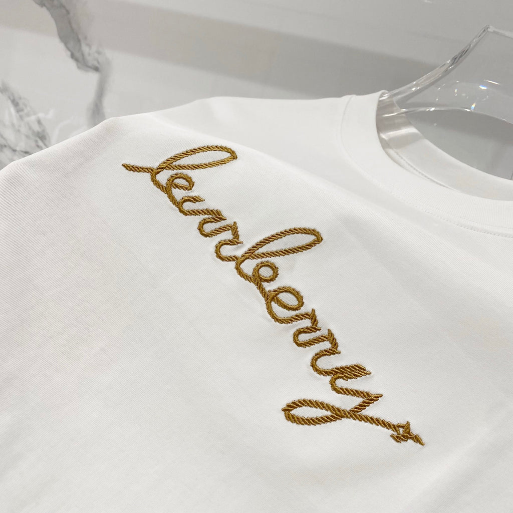 White short-sleeve T-shirt with gold embroidered logo text across the chest